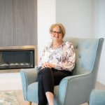 Robyn sitting in a duck egg blue fabric occasional chair in front of fireplace