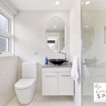 Beautiful white on white ensuite design with oval mirror above vanity